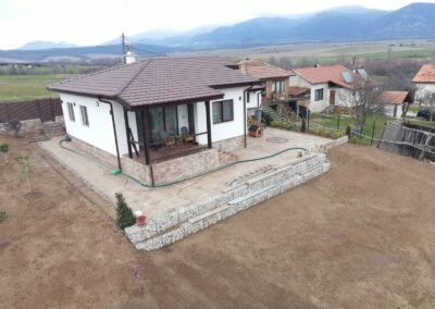 Страничен изглед към сглобяема къща с веранда, гараж и трискатен покрив с кафяви керемиди в с. Чавдар, проект на Хубав дом